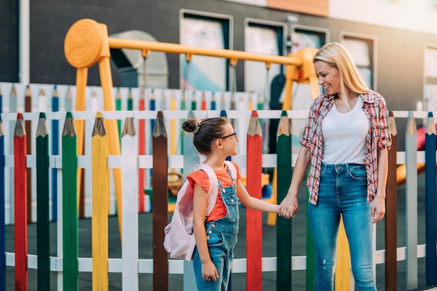 Jovem mãe caminhando com sua filha para a escola primária. De volta ao conceito de escola.