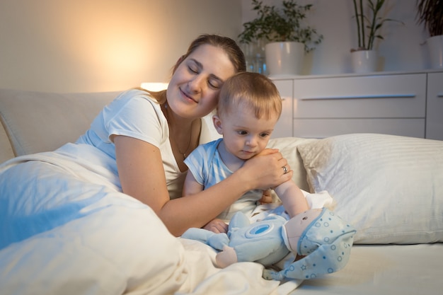 Jovem mãe carinhosa abraçando o bebê na cama à noite.