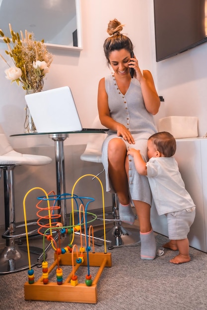 Jovem mãe caucasiana cuidando de seu filho e trabalhando em casa através de creches fechadas Falando ao telefone e na frente de um computador nova pandemia normal de coronavírus covid19