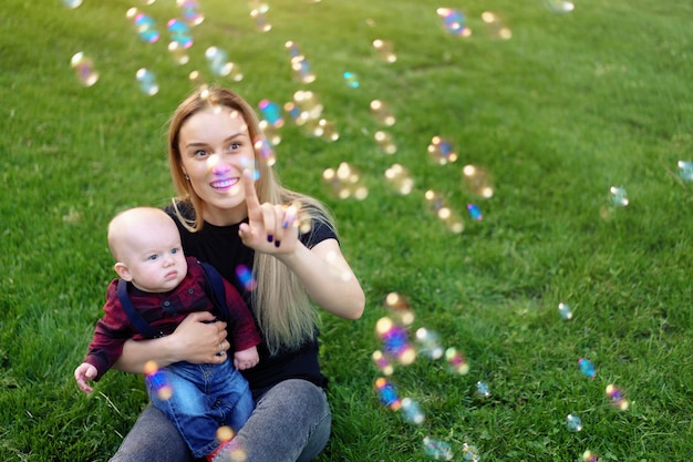 Jovem mãe caucasiana infla bolhas de sabão com seu filho pequeno em um parque em um dia ensolarado de verão.