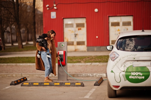 Jovem mãe com criança carregando eletro carro no posto de gasolina elétrico.