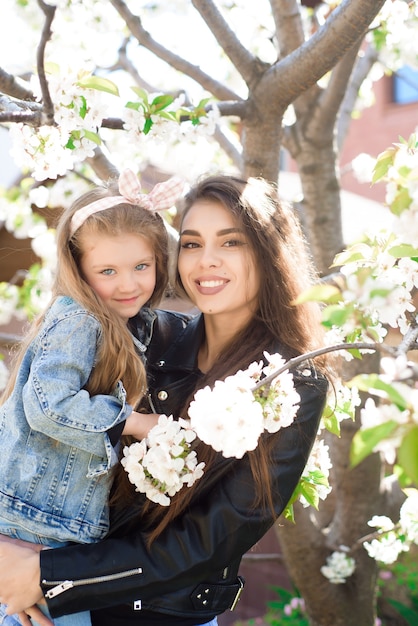 Jovem mãe com filha adorável no parque com árvore de flores