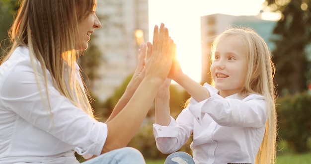 Jovem mãe com filha brincando de mãos dadas ao ar livre ao pôr do sol. horário de verão em um parque. família feliz