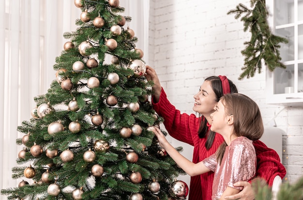 Jovem mãe com filha decoram juntos uma árvore de Natal festiva.