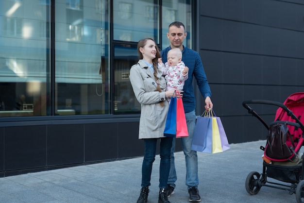 Jovem mãe com filha nos braços. pai com sacolas de compras na mão. compras em família.