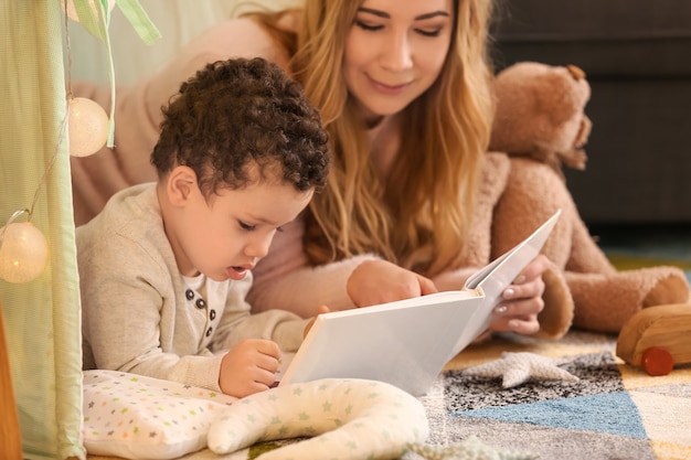 Jovem mãe com filho pequeno e fofo lendo livro em casa