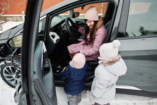 Jovem mãe com filhos carregando carro elétrico no quintal de sua casa no inverno