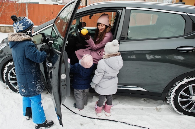 Jovem mãe com filhos carregando carro elétrico no quintal de sua casa no inverno
