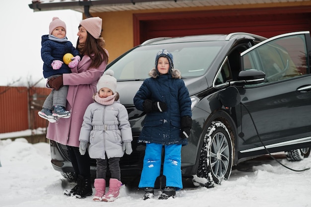 Jovem mãe com filhos carregando carro elétrico no quintal de sua casa no inverno