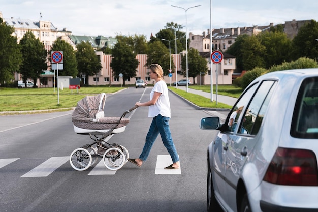 Jovem mãe com o carrinho de bebê está andando pela faixa de pedestres