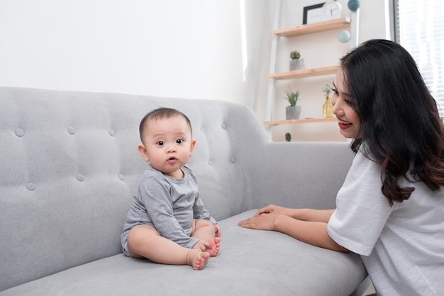 Jovem mãe com seu filhinho de um ano de pijama estão relaxando e brincando na sala no fim de semana juntos, manhã preguiçosa, cena quente e aconchegante. Foco seletivo.