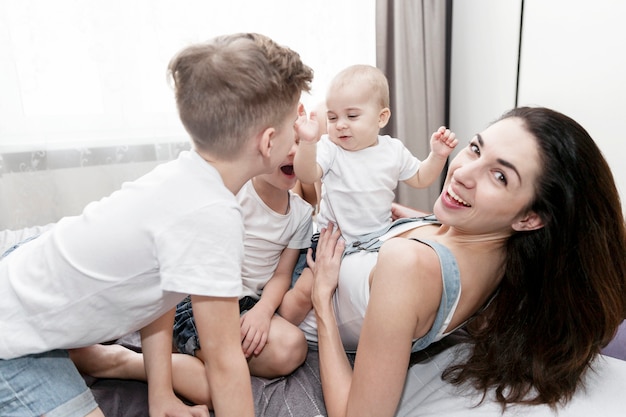 jovem mãe com seus filhos pequenos está deitada na cama e rindo. Ternura nas relações familiares.