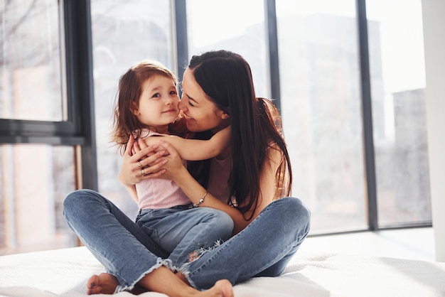 Jovem mãe com sua filha se abraçando na cama