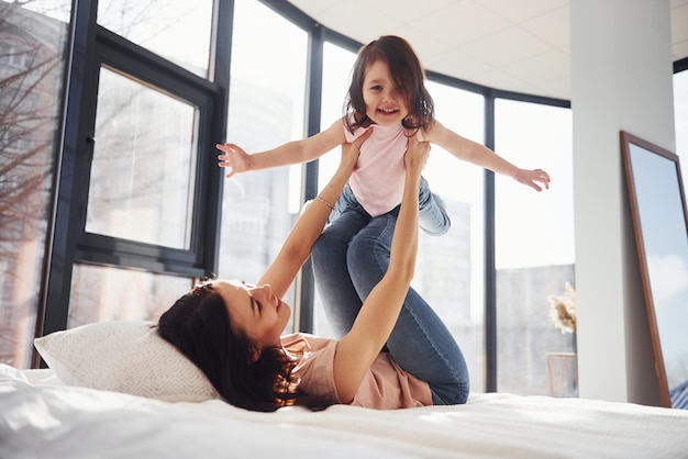 Jovem mãe com sua filha se diverte no fim de semana juntos na cama