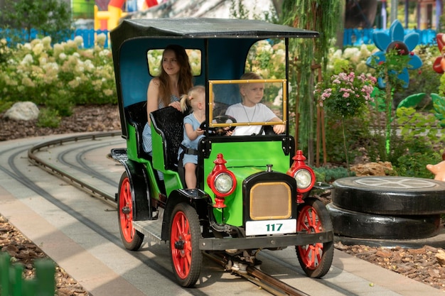 Jovem mãe e dois filhos andam de carro em um parque de diversões nanny anda com crianças no parque