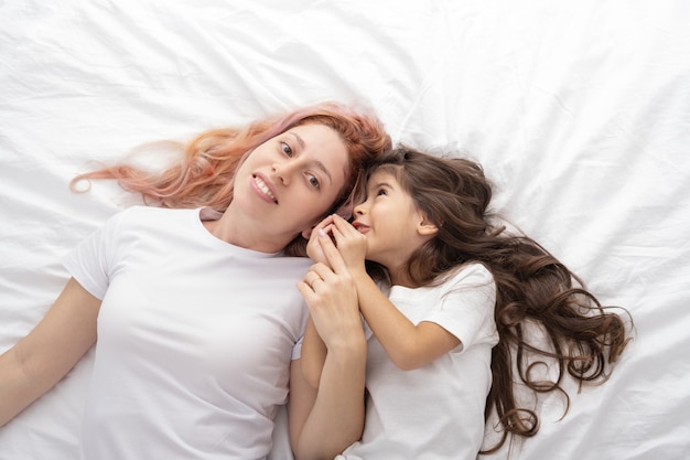 Jovem mãe e filha ativa deitada na cama em casa, se divertindo.