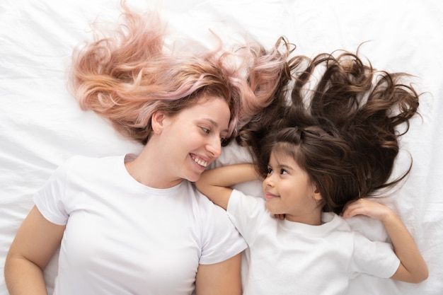 Foto jovem mãe e filha ativa deitada na cama em casa, se divertindo.