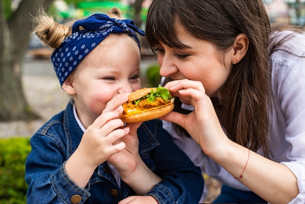 Jovem mãe e filha comendo hambúrguer de orelha juntas em um café ao ar livre