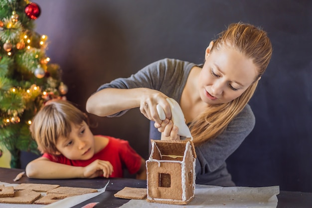 Jovem mãe e filha fazendo casa de pão de mel na véspera de Natal