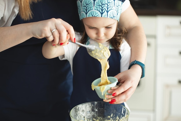 Jovem mãe e filha na cozinha despejam a massa para os cupcakes em formas. fechem as mãos.