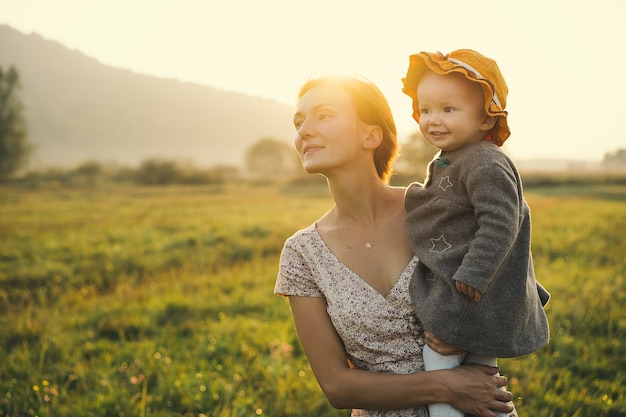 Jovem mãe e filha na luz do sol ao pôr do sol na natureza ao ar livre Mãe e filho no prado