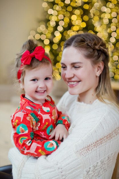 Jovem mãe e filha perto da árvore de Natal Família feliz esperando pelo Natal e Ano Novo Interior leve aconchegante com luzes e decorações de Natal