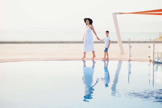 Jovem mãe e filho caminhando perto da piscina.