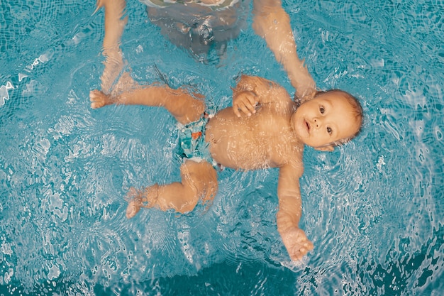 Jovem mãe e seu bebê, desfrutando de uma aula de natação do bebê na piscina. Criança se divertindo na água com a mãe