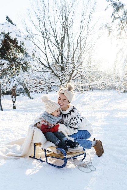 Foto jovem mãe e seu filho bonitinho com trenó retrô em um parque nevado durante o dia ensolarado de inverno