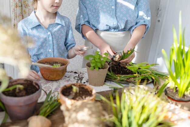 Foto jovem mãe e sua filha pequena em looks de família vestidos estão plantando flores no terraço de primavera em casa jardim mudas crescendo casa de campo varanda maternidade