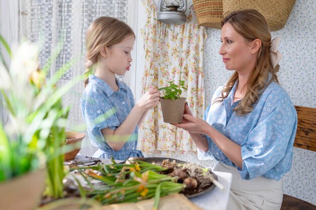 Foto jovem mãe e sua filha pequena em looks de família vestidos estão plantando flores no terraço de primavera em casa jardim mudas crescendo casa de campo varanda maternidade