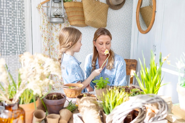 Foto jovem mãe e sua filha pequena em looks de família vestidos estão plantando flores no terraço de primavera em casa jardim mudas crescendo casa de campo varanda maternidade