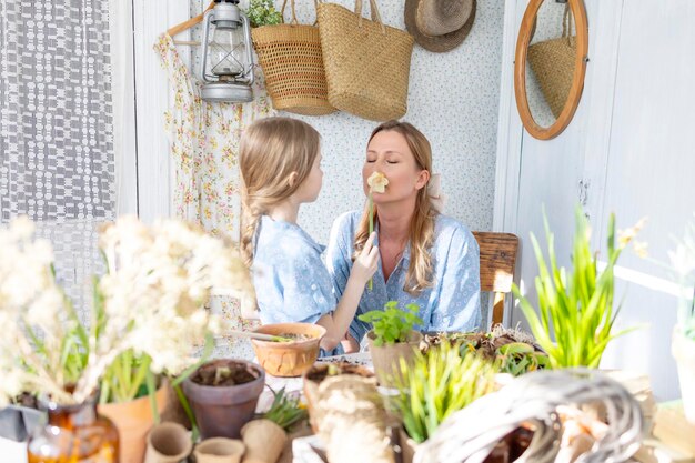 Jovem mãe e sua filha pequena em looks de família vestidos estão plantando flores no terraço de primavera em casa jardim mudas crescendo casa de campo varanda maternidade