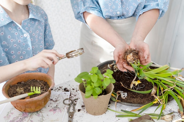 Foto jovem mãe e sua filha pequena em looks de família vestidos estão plantando flores no terraço de primavera em casa jardim mudas crescendo casa de campo varanda maternidade