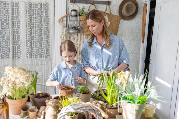 Jovem mãe e sua filha pequena em looks de família vestidos estão plantando flores no terraço de primavera em casa jardim mudas crescendo casa de campo varanda maternidade