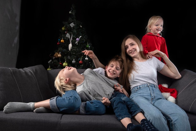 Jovem mãe e três filhos no sofá contra no fundo da árvore de natal. família feliz.