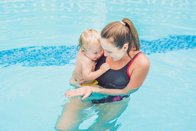 Jovem mãe ensina seu filho pequeno, como nadar em uma piscina
