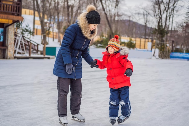 Jovem mãe ensinando seu filho pequeno a patinar no gelo na pista de patinação ao ar livre Família aproveita o inverno na pista de gelo ao ar livre