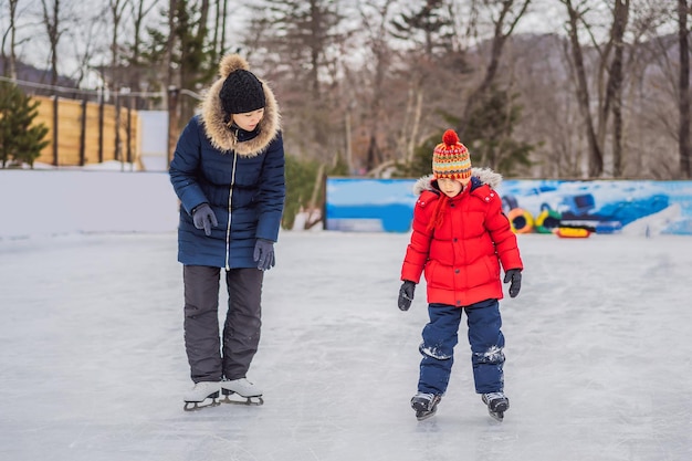 Jovem mãe ensinando seu filho pequeno a patinar no gelo na pista de patinação ao ar livre Família aproveita o inverno na pista de gelo ao ar livre