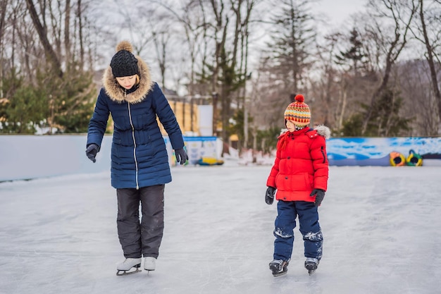 Jovem mãe ensinando seu filho pequeno a patinar no gelo na pista de patinação ao ar livre Família aproveita o inverno na pista de gelo ao ar livre