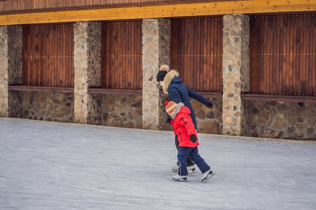 Jovem mãe ensinando seu filho pequeno a patinar no gelo na pista de patinação ao ar livre Família aproveita o inverno na pista de gelo ao ar livre