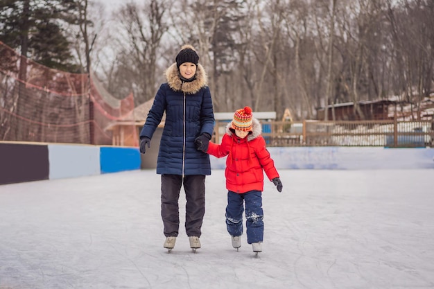 Jovem mãe ensinando seu filho pequeno a patinar no gelo na pista de patinação ao ar livre Família aproveita o inverno na pista de gelo ao ar livre