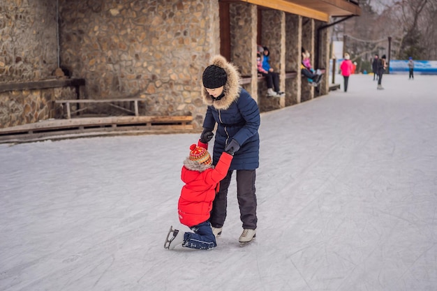 Jovem mãe ensinando seu filho pequeno a patinar no gelo na pista de patinação ao ar livre Família aproveita o inverno na pista de gelo ao ar livre