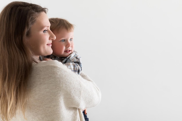 Jovem mãe europeia com um bebê em abraços em um fundo branco ambos olham em um espaço de cópia de direção