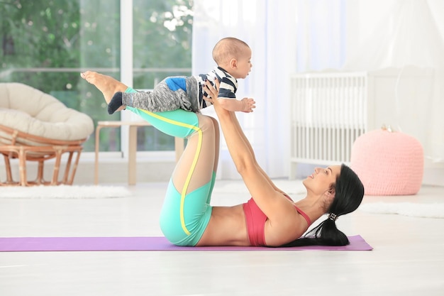 Jovem mãe fazendo exercícios enquanto segura o bebê em casa