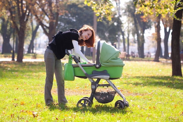 Jovem mãe feliz carregando um bebê no parque outono