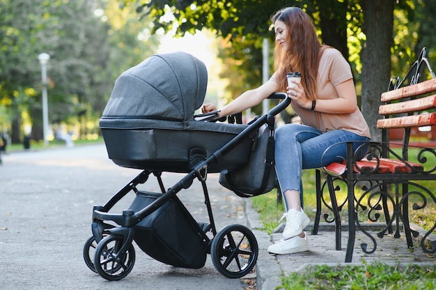 Jovem mãe feliz com bebê em carrinho sentado no banco do parque outono