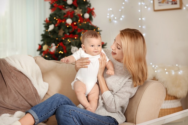 Jovem mãe feliz com bebê em quarto decorado para o Natal