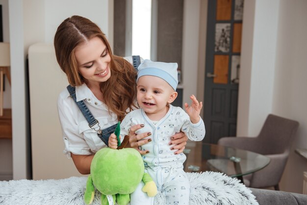 Jovem mãe feliz segurando e brincando com seu filho pequeno com um brinquedo em casa