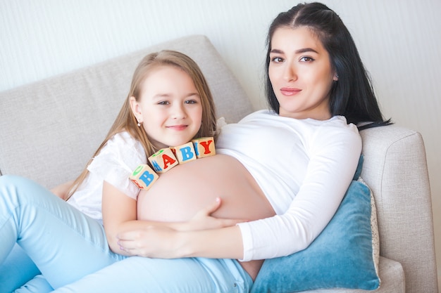 Jovem mãe grávida e sua filha dentro de casa.